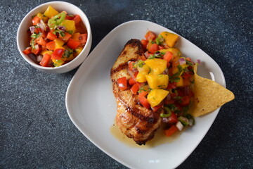 Grilled chicken breast with spicy salsa salad, mango, herbs, onions and peppers, corn chips. Mexican Food.