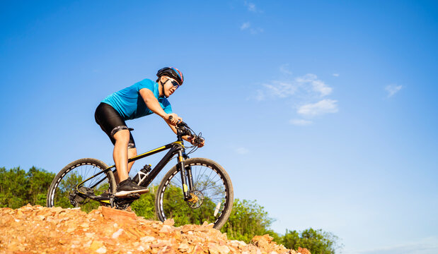 Mountain bikes cyclist cycling, Asian man athlete riding biking on rocky terrain trail, extreme sport wearing gear uniform helmet, exciting joy freedom outdoor sunset nature healthy active lifestyle