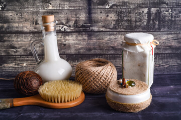 the lay composition with body care products on dark wood background. A jar of natural cream, a bottle of coconut and brush for washing