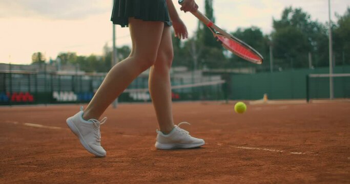 slow-motion side view of a young athlete trains the serve of the tennis ball. A teenage athlete is playing tennis on a court. An active girl is powerfully hitting a ball during sport practicing