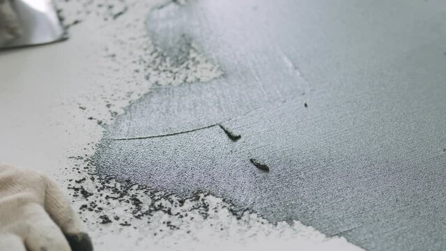 Slow motion pan closeup male worker applying micro concrete plaster coating on the floor with a trowel