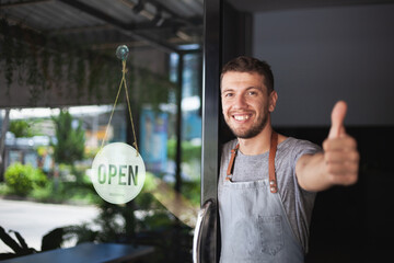 Young Chef owner of sushi restaurant smiling while turning the sign for the reopening of his place...
