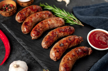 grilled sausages with spices on a slate board on a stone background