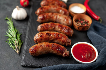 grilled sausages with spices on a slate board on a stone background