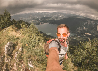 Young man with a beard taking a selfie with a landscape behind him.