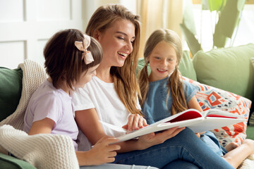 Children spend time at home with their parents reading a book on the sofa