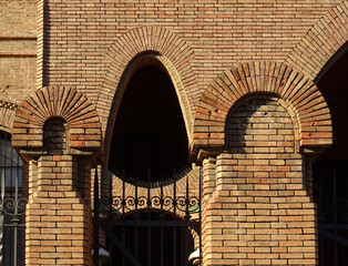 Detail of Revival metallic and brick fence and wall with catenary arch. Old city center of Tarragona. Catalonia. Spain. 