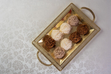Brazilian cocada (coconut candy) placed on a golden tray on a table with white towel, selective focus.