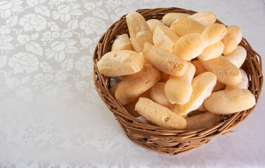 Traditional Brazilian starch biscuit called biscoito de polvilho in a basket on a table covered with white tablecloth, selective focus.