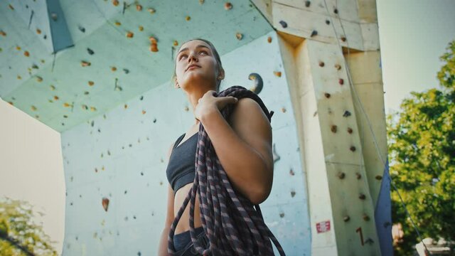 Young girl alpinist holding climbing rope at outdoor gym wall, tracking shot