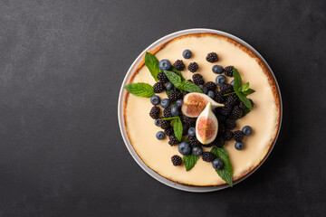 Delicious cheesecake with fresh berries, mint and figs in a white plate on a dark background.