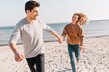 Joyful girl in jeans expressing positive emotions during photoshoot at sea. Outdoor photo of lovable lady enjoying rest at beach.