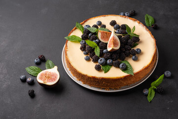 Delicious cheesecake with fresh berries, mint and figs in a white plate on a dark background.