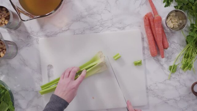 Curring vegetables on a white cutting board to cook vegetarian white bean soup.