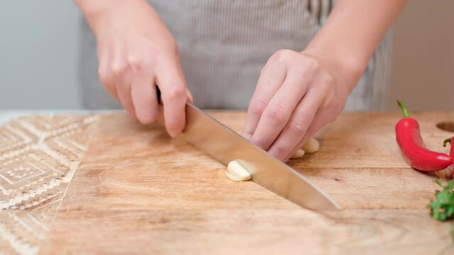 Close-up chopping garlic with a chef knife in 4K. Concept of cutting/slicing garlic on a cutting board in slow motion.