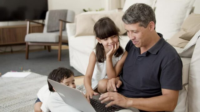 Cheerful kids interrupting dads work with laptop, and playing with keyboard. Home office and parenthood concept