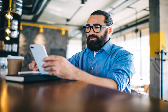 Smiling Prosperous Caucasian Male Owner Of Small Business Sitting Near Bar Checking Mail On Mobile Phone, Positive Maturen 40 Years Man Reading News And Share Media Using Smartphone Connected To 4G