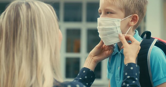 Boy, schoolboy in protective mask goes to school. Mother helps her son put on protective mask. 4K video
