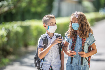 Two young friends classmates with face masks talk on their way to school during the Covid-19 quarantine