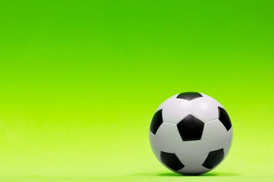 Soccer ball isolated against a plain green background with gradual color shading. Conceptual image with copy space on the left side.