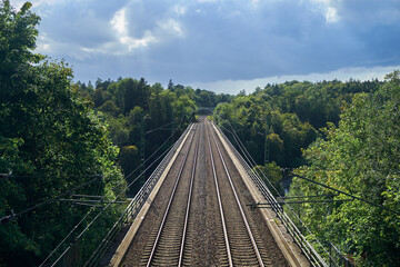 Railway tracks are photographed from above. Railway tracks are surrounded by green trees