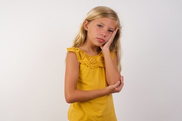 Very bored adult Little blond girl wearing yellow dress over white background. holding hand on...