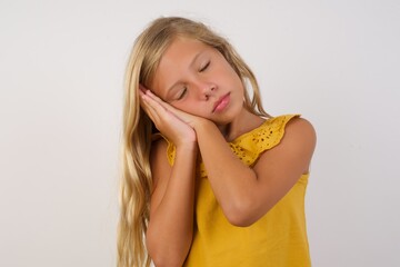 Little blond girl wearing yellow dress over white background sleeping tired dreaming and posing...