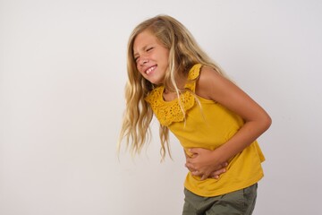 Young blonde kid girl wearing yellow dress over white background with hand on stomach because...