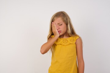 Young blonde kid girl wearing yellow dress over white background Yawning tired covering half face, eye and mouth with hand. Face hurts in pain.