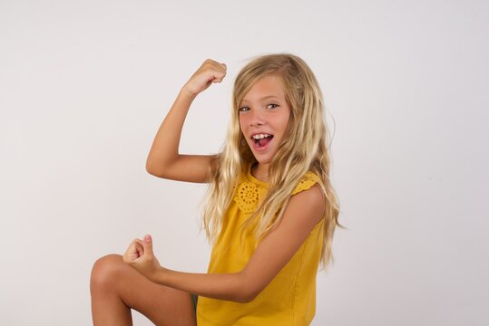 Profile photo of excited Little girl with beautiful blonde hair over white background raising fists celebrating black friday shopping