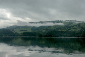 Mountains and hills reflecting in the clear water of lake - hazy clouds on the sky