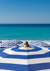 Obraz premium Nahaufnahme eines blau weiß gestreiften Sonnenschirms am Strand mit blauem Meer und weiteren Sonnenschirmen im Hintergrund