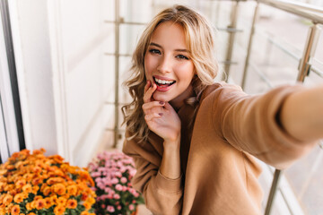 Debonair young woman making selfie at balcony. Photo of smiling dreamy girl posing beside orange...