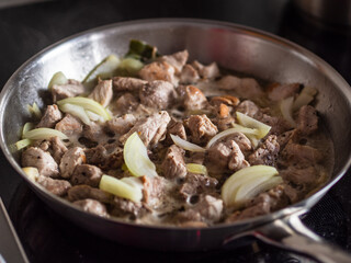 Pork nuggets frying in pan with white onion