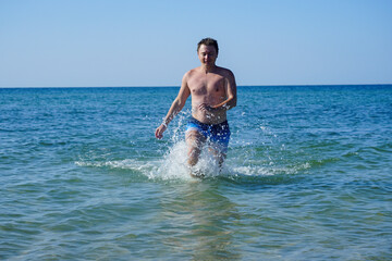 The guy runs along the waves in the sea with azure water. Splashes fly to the sides