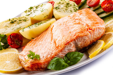 Fried salmon steak with potatoes and vegetables on white background
