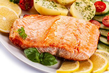 Fried salmon steak with potatoes and vegetables on white background