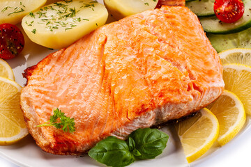 Fried salmon steak with potatoes and vegetables on white background