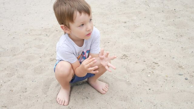 A lovely little boy sitting on the beach and playing with sand