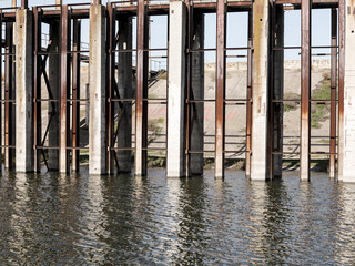 Rusty metal and concrete structures on river. Old abandoned metal structure on stilts in the water in the shallow water.