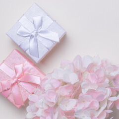 Festive greeting square poster for a postcard, gift wrapping, beautiful silver box with a bow of ribbons for the holiday on a peach background with a pink artificial hydrangea flower top view, flatlay