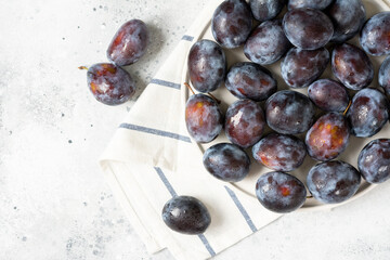 Ripe plum. A lot of plums in a white ceramic plate on a light gray table. Blue plums on a plate. Top view with space for text. Healthy fruits	