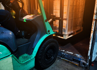 Worker driving forklift loading shipment carton boxes goods on wooden pallet at loading dock from...