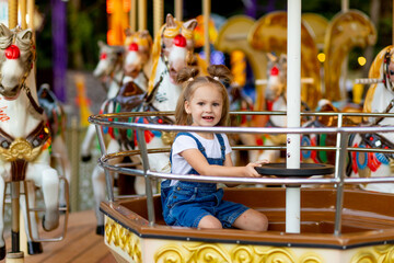 happy baby girl riding on carousel at an amusement Park in the summer