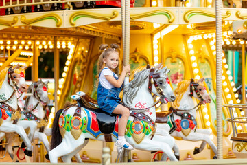 Fototapeta na wymiar happy baby girl rides a carousel on a horse in an amusement Park in summer