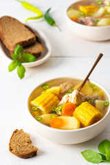 Delicious hearty lunch, soup with chicken and rice, sweet boiled corn ,green onions and potato in a plate on the table with bread, beautiful bouquet of flowers in a vase