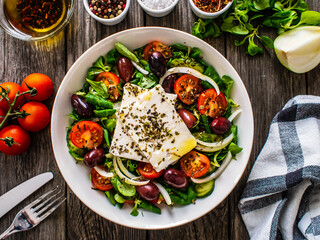 Fresh Greek salad - feta cheese, tomatoes, cucumber, red pepper, black olives and onion on wooden table