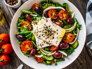 Fresh Greek salad - feta cheese, tomatoes, cucumber, red pepper, black olives and onion on wooden table