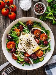 Fresh Greek salad - feta cheese, tomatoes, cucumber, red pepper, black olives and onion on wooden table