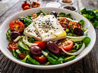 Fresh Greek salad - feta cheese, tomatoes, cucumber, red pepper, black olives and onion on wooden table